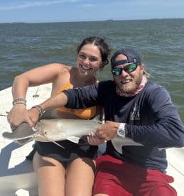 Two anglers proudly displaying a caught shark while enjoying a sunny day on the water.