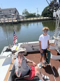 A father and son relaxing on the deck of a fishing boat, preparing for a day on the water, with fishing rods visible in the background.