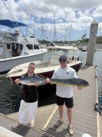 Two anglers proudly displaying their catches, a Mahi Mahi and a Bonito, at the marina after a successful fishing trip.