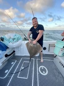 An angler proudly displaying a large stingray aboard a fishing boat, showcasing the excitement of a successful catch during a day on the water.