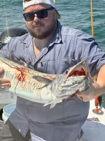 An angler proudly displaying a large King Mackerel on a sunny day while fishing offshore.
