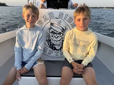 Two young boys seated inside a fishing boat, enjoying the day on the water with a scenic backdrop.
