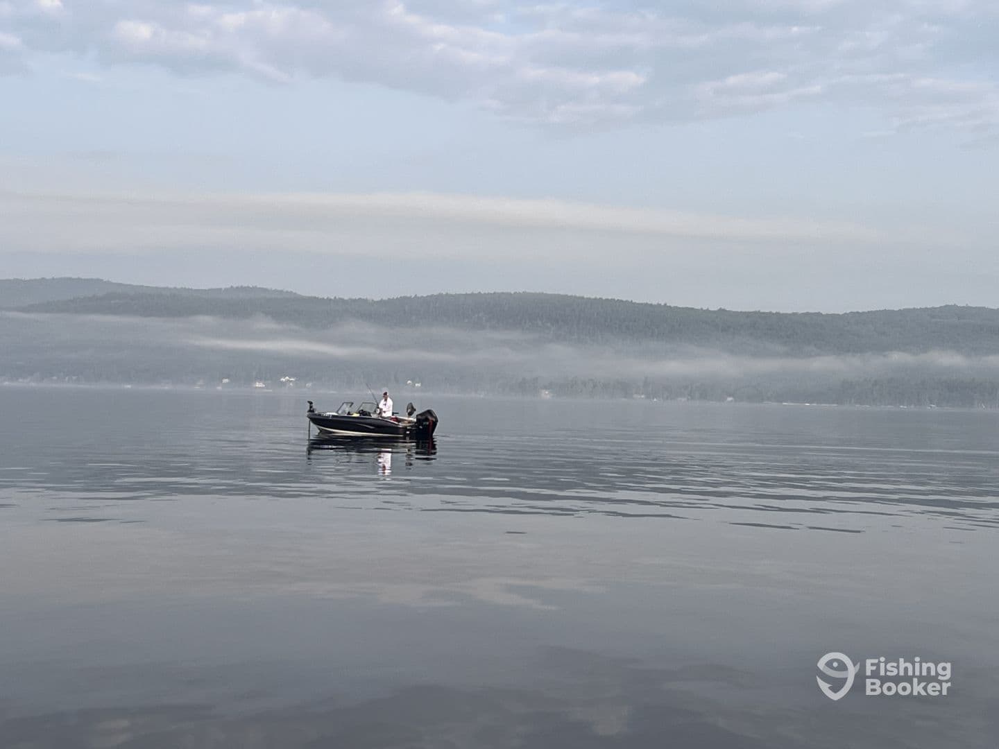 A fishing boat is seen gliding across a calm lake, surrounded by misty hills, creating a serene fishing environment.