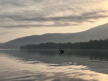 A serene morning scene featuring a fishing boat on calm waters, surrounded by misty mountains, perfect for a tranquil fishing experience.