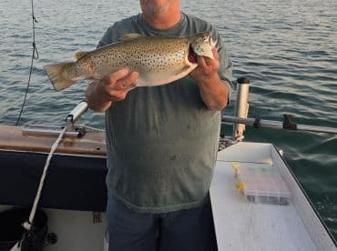 An angler proudly displaying a large Brown Trout while fishing from a boat in calm waters.