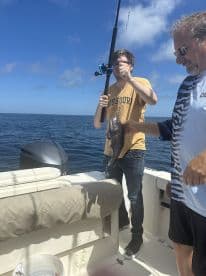 A young angler reeling in a Black Grouper while fishing on a boat in open waters, showcasing an exciting moment on the trip.