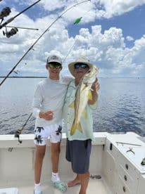 A young angler and an adult proudly displaying a large Snook on a fishing boat, enjoying a day on the water.