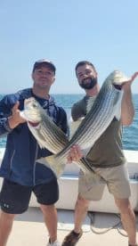 Two anglers proudly displaying their catch of striped bass while on a fishing trip.