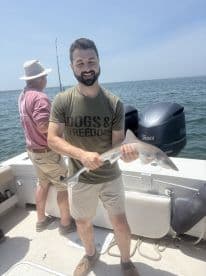 An angler proudly displaying a caught shark while fishing on a boat in open waters.