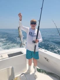 A young angler proudly displaying a Spanish Mackerel while fishing off the coast of Sandbridge Beach, Virginia.