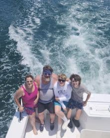 A family enjoying a day on a fishing boat, with two children and two adults posing together against the backdrop of the ocean.