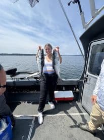 A young woman proudly displaying two large salmon on a fishing boat, enjoying a successful day on the water.