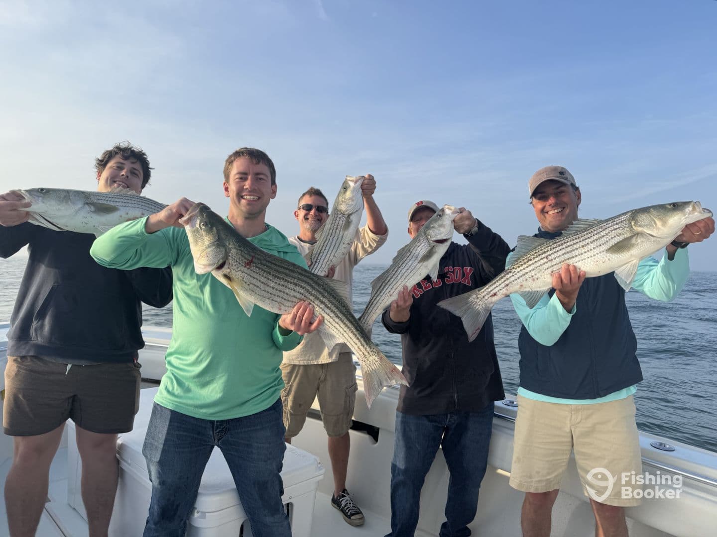 Group of anglers proudly displaying their catch of striped bass aboard a fishing boat, showcasing a successful day on the water.