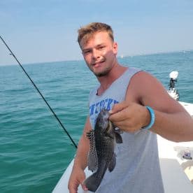 A young angler proudly displaying a Black Sea Bass while fishing on a boat in clear waters.