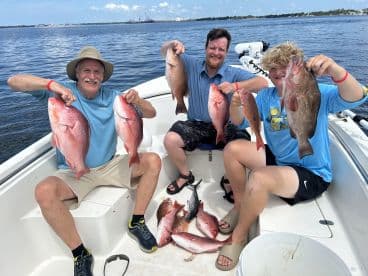 A group of anglers proudly displaying their catch of Red Snapper and a Grouper aboard a fishing boat, enjoying a successful day on the water.