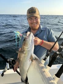 A proud angler holding a large fish while fishing in open waters, showcasing a successful catch during a deep-sea fishing trip.
