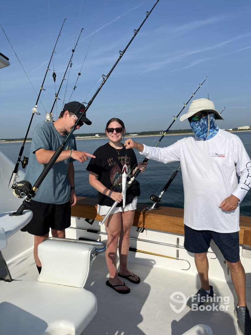 A young angler and her friend proudly display their catch on a fishing charter, surrounded by fishing rods on a sunny day.