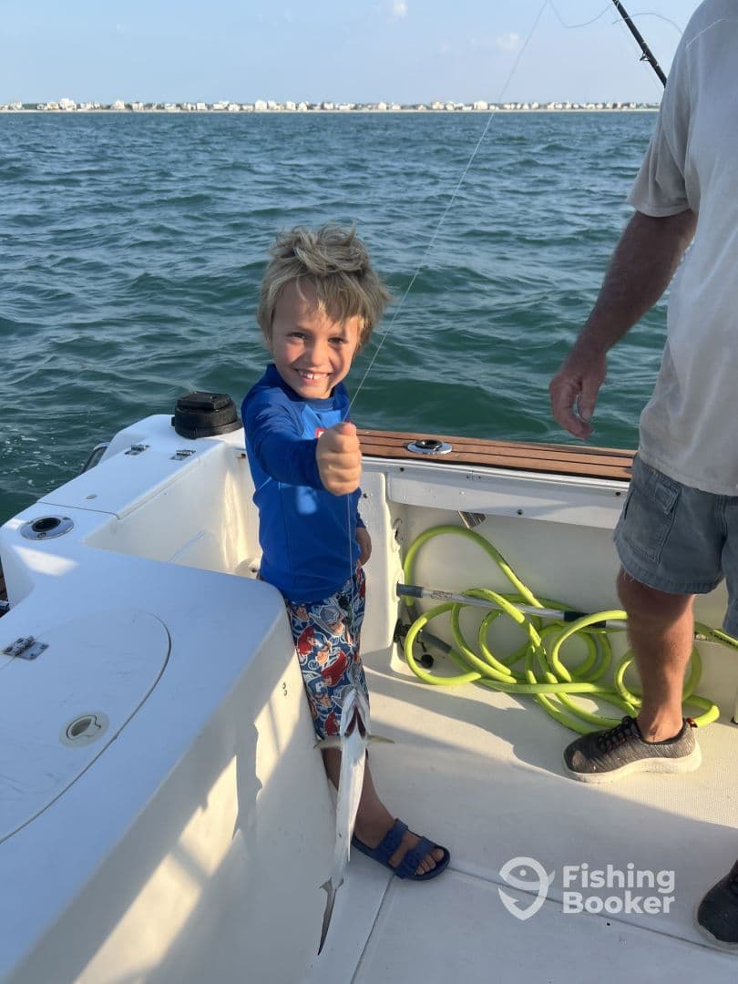 A young angler excitedly reeling in a fish while fishing on a boat, showcasing a fun family fishing experience.