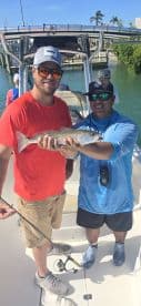 Two anglers proudly displaying a Speckled Trout on a sunny day while fishing from a boat.