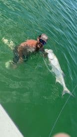 Angler enjoying a successful catch while holding a large Tarpon in the clear waters, showcasing the excitement of inshore fishing.