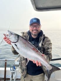 An angler proudly displaying a freshly caught fish while aboard a fishing boat in a foggy marine environment.