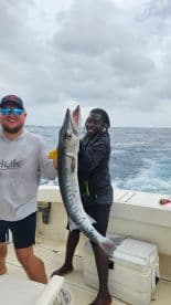 Two anglers proudly displaying a large Barracuda on a fishing charter in open waters.