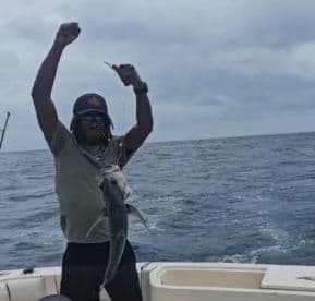 Angler celebrating a successful catch of a large fish while out on the open ocean, showcasing the thrill of deep-sea fishing.