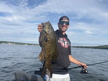 A proud angler displaying a large Smallmouth Bass while fishing on a serene lake, showcasing a perfect day for fishing.