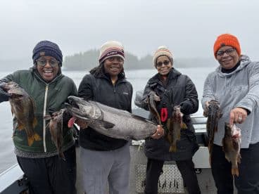 A group of four anglers proudly displaying their catch, including a large salmon and several other fish, while enjoying a fishing trip in Alaska.