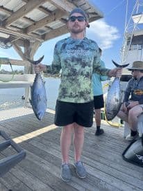 Angler proudly displaying two large fish, likely Tuna, at the dock after a successful fishing trip.