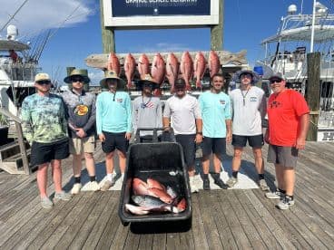 A group of anglers proudly posing with their catch of Red Snapper displayed on a board at the dock, showcasing a successful fishing trip.