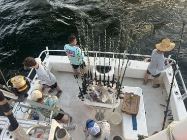 A group of young anglers actively fishing from a charter boat, showcasing multiple fishing rods and a lively fishing environment.