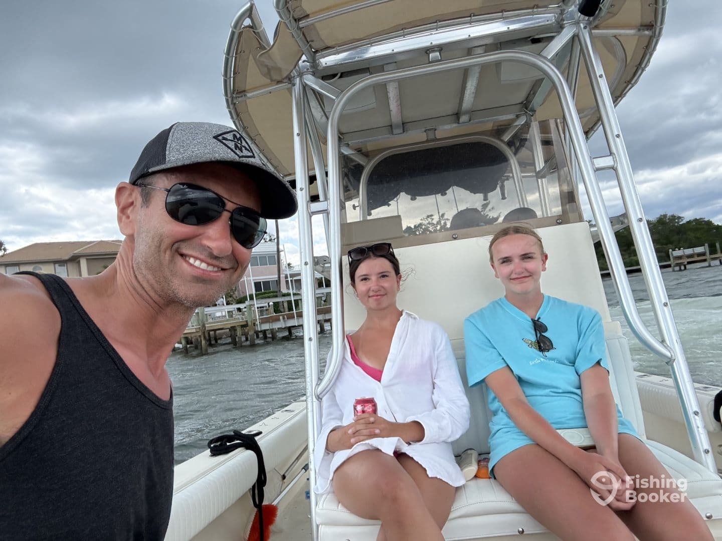 A group of three individuals enjoying a day on a center console boat, with a scenic waterfront in the background.
