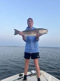 A young angler proudly displaying a large Redfish while fishing on a calm waterway.