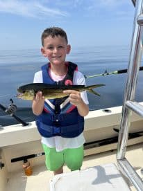 Young angler proudly holding a small Mahi Mahi while fishing on a calm day at sea.