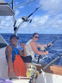 Two anglers enjoying a fishing trip on a boat, actively reeling in lines while surrounded by the open ocean.