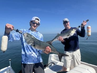 A young angler and an adult proudly displaying their catch of Bluefish while on a fishing trip in calm waters.
