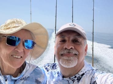 A couple enjoying a fishing trip on a boat, with fishing rods visible in the background and a clear view of the ocean.