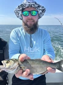 Angler proudly displaying a caught fish while on a boat in open waters, showcasing a sunny day of fishing.