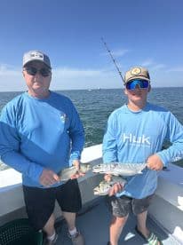 A young angler and an adult proudly displaying their catch of fish while out on a fishing charter in clear waters.