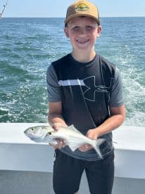 A young angler proudly displaying a freshly caught fish while aboard a fishing boat, enjoying a sunny day on the water.