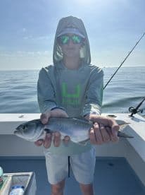 A young angler proudly displaying a caught fish while fishing on a boat in calm waters.