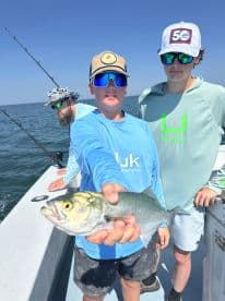 A young angler proudly displaying a caught fish while fishing with friends on a sunny day at sea.