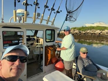 Two anglers are aboard a fishing boat, with one at the helm and another seated, enjoying a calm morning on the water.