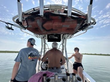 Three individuals aboard a center console boat, enjoying a calm day on the water, with a scenic view of the marshlands.