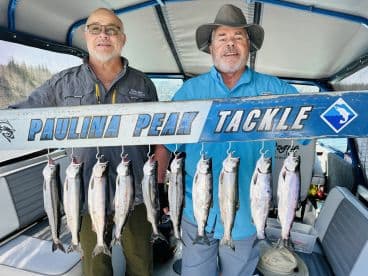 Two anglers proudly displaying a catch of multiple trout on a board inside a fishing boat, showcasing their successful day on the water.