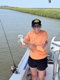 An angler proudly displaying a small shark while fishing in a scenic marsh environment.