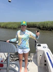 Young angler proudly holding a catfish while standing on a boat in a marshy fishing environment.