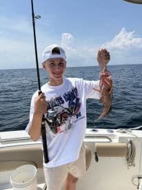 A young angler proudly displaying a caught fish while fishing on a boat in open waters.