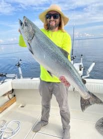Angler proudly displaying a large Salmon while fishing on a calm day, showcasing the excitement of a successful catch.